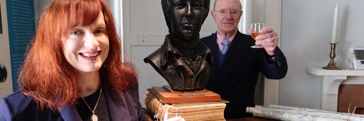 Man and woman with a dram of whisky alongside bust of Robert Burns